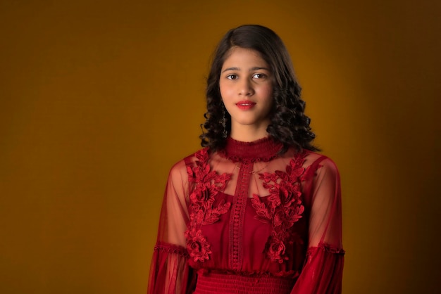 Linda chica joven con un hermoso vestido rojo posando sobre fondo marrón