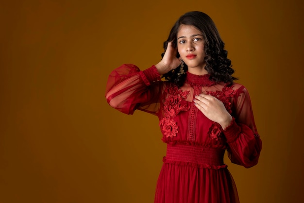 Linda chica joven con un hermoso vestido rojo posando sobre fondo marrón