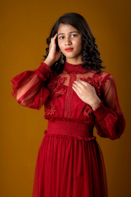 Linda chica joven con un hermoso vestido rojo posando sobre fondo marrón