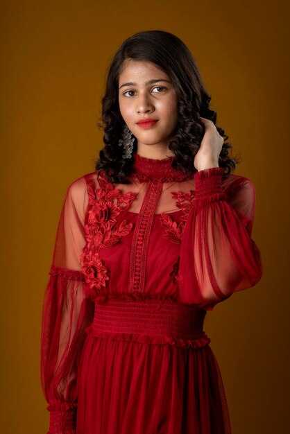 Linda chica joven con un hermoso vestido rojo posando sobre fondo marrón