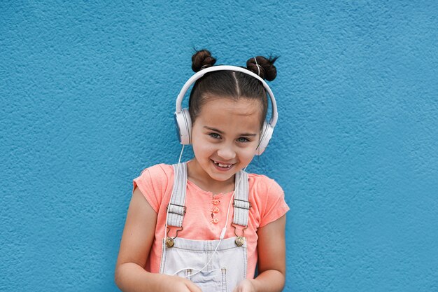 Linda chica joven mirando a la cámara mientras escucha la lista de reproducción de música con auriculares - Concepto de niño y tecnología