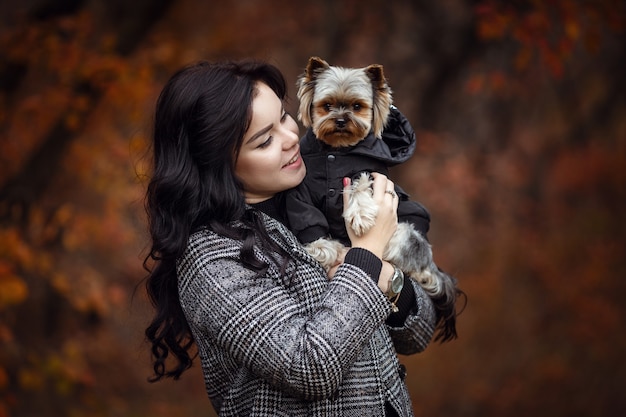 Linda chica joven con perro yorkshire terrier en el parque en otoño. concepto de cuidado y amistad