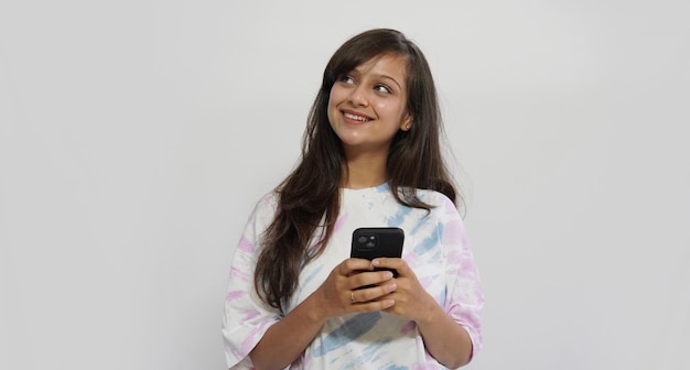 Foto linda chica joven positiva soñando sobre fondo de pared gris usando un teléfono móvil.