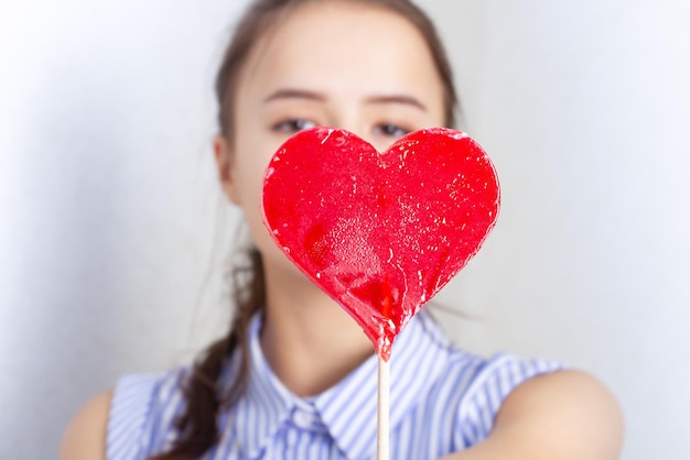 Linda chica joven se ríe, comiendo una piruleta en forma de corazón