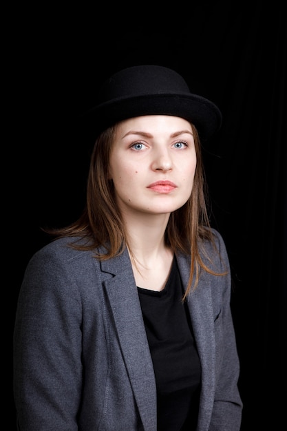 Foto linda chica joven con sombrero y chaqueta gris sobre fondo negro