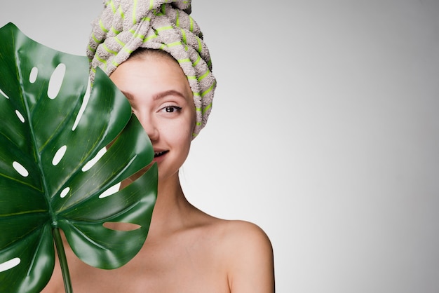 Foto linda chica joven con una toalla en la cabeza disfrutando de tratamientos de spa, sosteniendo una hoja verde