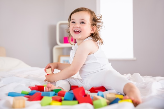 Linda chica jugando con bloques de construcción en la cama