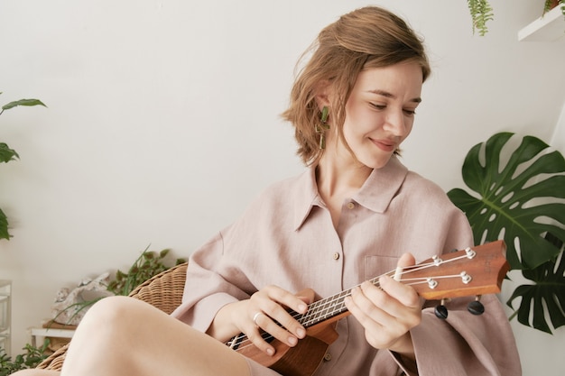 Linda chica jugando en casa con el ukelele