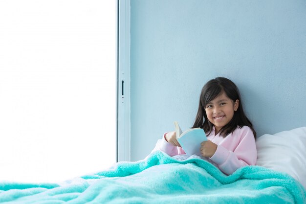 Linda chica latina en la cama leyendo un libro antes de dormir