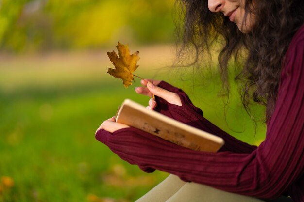 Una linda chica lee un libro y bebe café en un césped verde en un parque de otoño. Estado de ánimo de otoño. Un lugar acogedor para estar a solas contigo mismo.