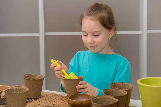 Linda chica en la mesa prepara macetas de turba para plantar plántulas