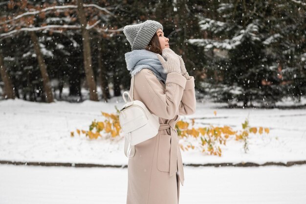 Una linda chica con una mochila está parada bajo la nieve.