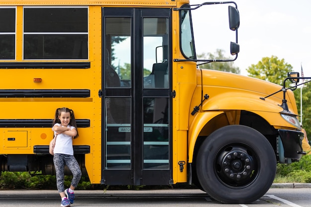 Linda chica con una mochila de pie cerca del autobús que va a la escuela posando para la cámara pensativo primer plano