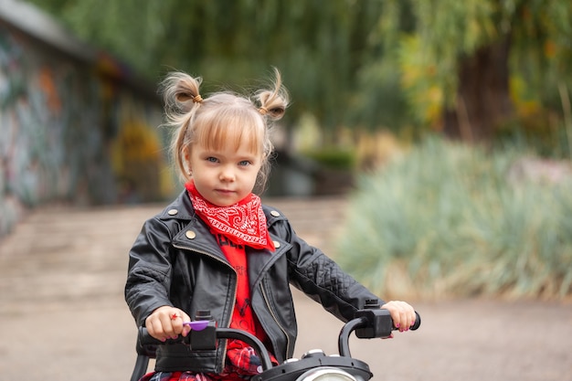 Linda chica de moda niño fresco en chaqueta de cuero montando la moto