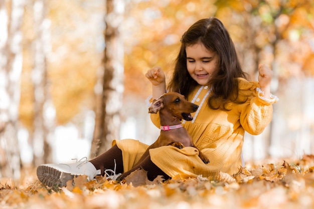 Una linda chica morena camina en otoño con un perro dachshund en el parque