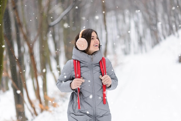 Linda chica morena considerando los paisajes invernales mientras camina en el bosque nevado con mochila