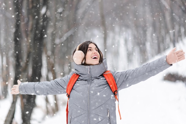 Linda chica morena se regocija de la nieve mientras camina en el bosque nevado con mochila