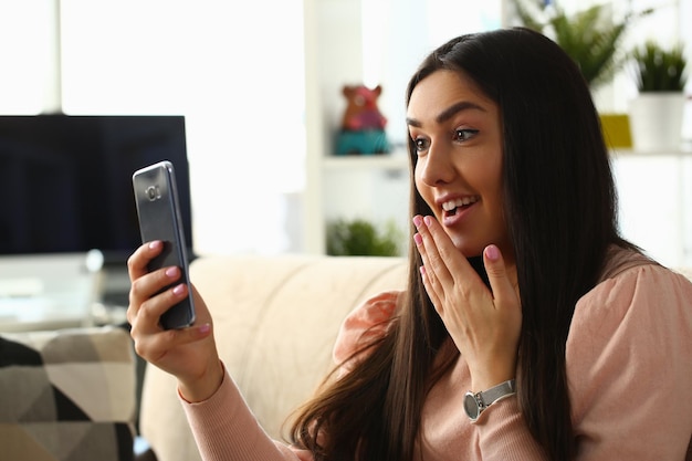 Linda chica morena se toma selfie en el teléfono inteligente expresa sorpresa por el contenido de la imagen para las redes sociales