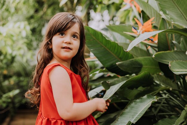 una linda chica morena en un vestido rojo camina en verano entre las palmeras en el parque