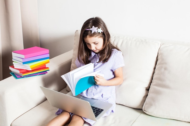 A la linda chica se le ocurrió una idea. La niña sentada en el sofá con laptop y libros