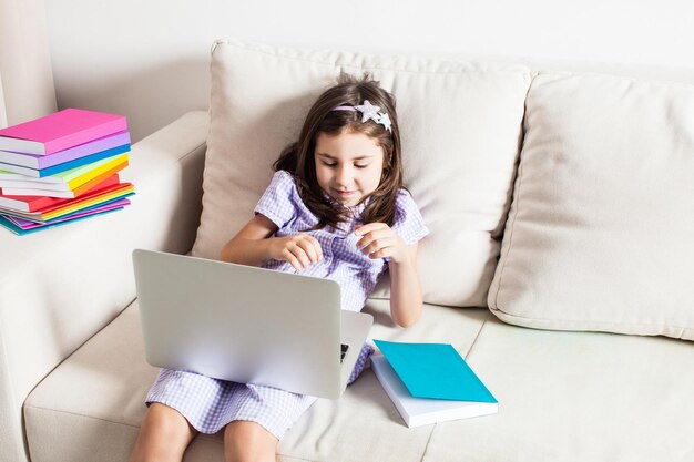 A la linda chica se le ocurrió una idea. La niña sentada en el sofá con laptop y libros