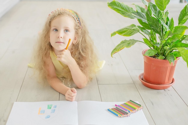 una linda chica con ojos azules dibuja una planta de interior junto a ella en un álbum con lápices de colores