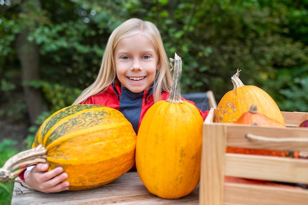 Una linda chica parada cerca de la mesa con calabazas en