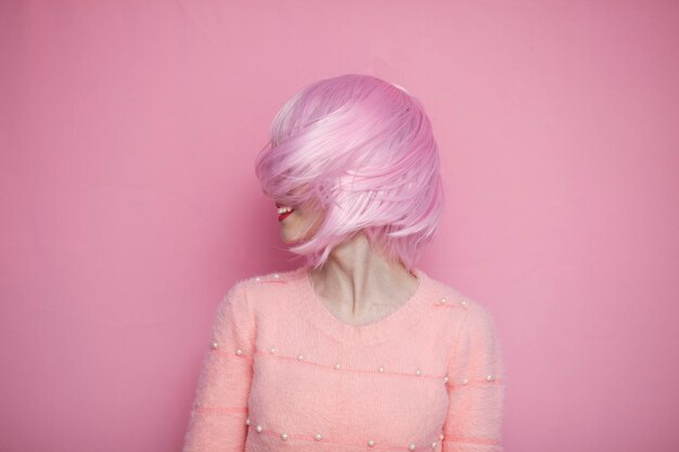 Foto linda chica con el pelo rosa gira la cabeza hacia un lado y sonríe, el pelo corto, ligero y delicado vuela sobre un fondo rosa