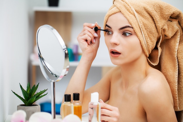 Linda chica pone maquillaje en la cara en el baño