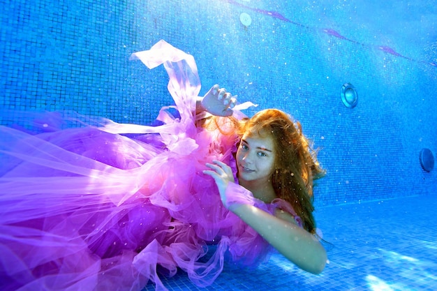 Linda chica posando bajo el agua con un hermoso vestido en el fondo de una piscina al aire libre