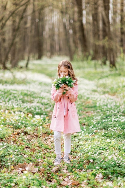 Linda chica con un ramo de campanillas en el bosque de primavera. Un niño huele flores