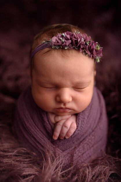 Foto linda chica recién nacida durmiendo en un flocket púrpura en una envoltura de color púrpura.