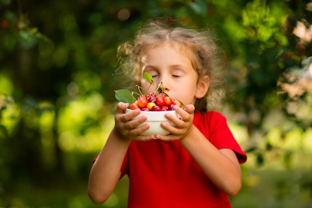 Una linda chica recoge cerezas en el jardín al atardecer Productos ecológicos de verano