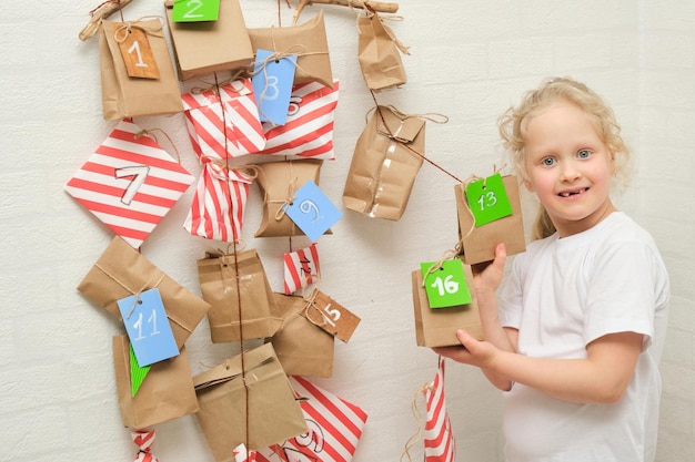 Linda chica rizada con cabello rubio y una niña y un calendario de eventos colgado en la pared la víspera de navidad