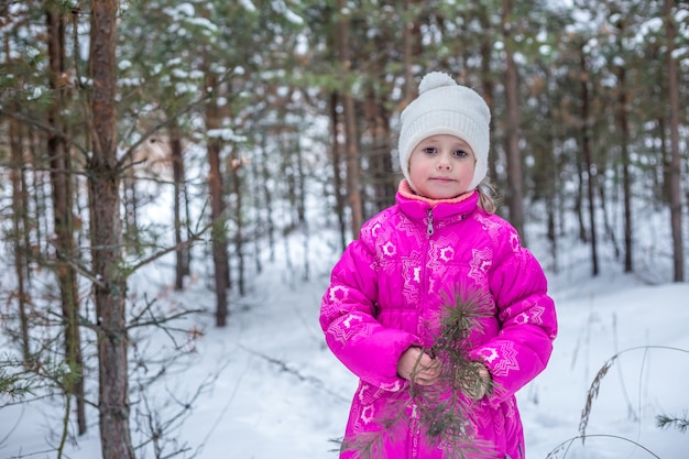 Linda chica en ropa de abrigo rosa jugando en el bosque de invierno, pasar tiempo al aire libre en invierno