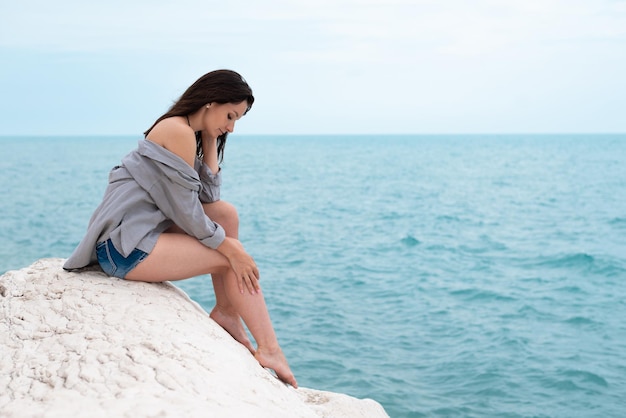 Linda chica con ropa de verano en una roca blanca en la costa del mar