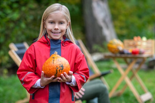 Una linda chica rubia con una calabaza en las manos.