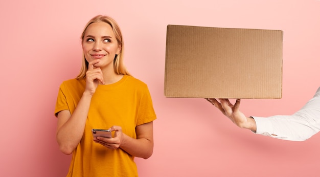 Linda chica rubia conectada a Internet recibe una caja del pedido de una tienda en línea