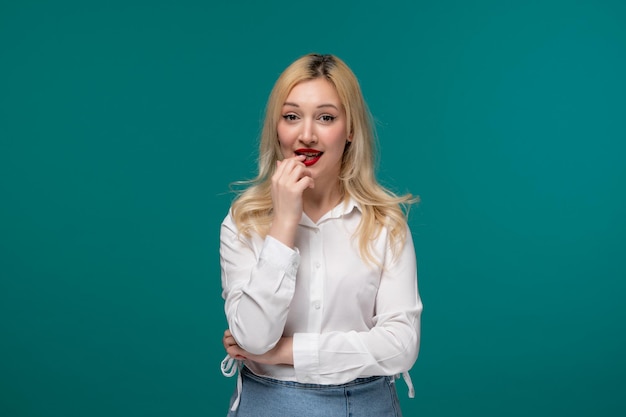 Linda chica rubia joven bonita en una camisa blanca mordiendo el dedo y emocionada