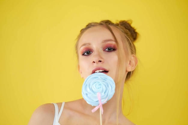 Linda chica rubia con lolipop sobre fondo amarillo divertido peinado