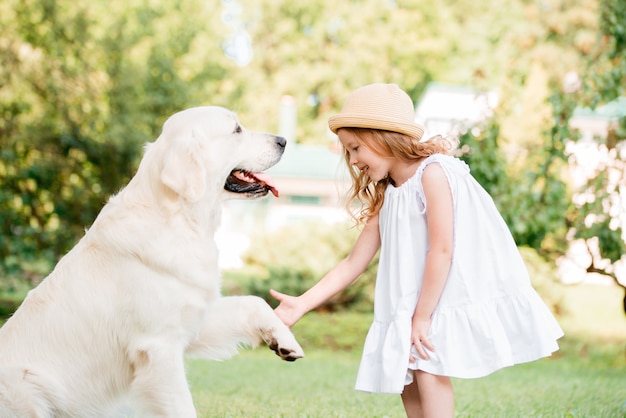 Una linda chica rubia con ojos azules y un gran perro blanco en un parque soleado de verano.