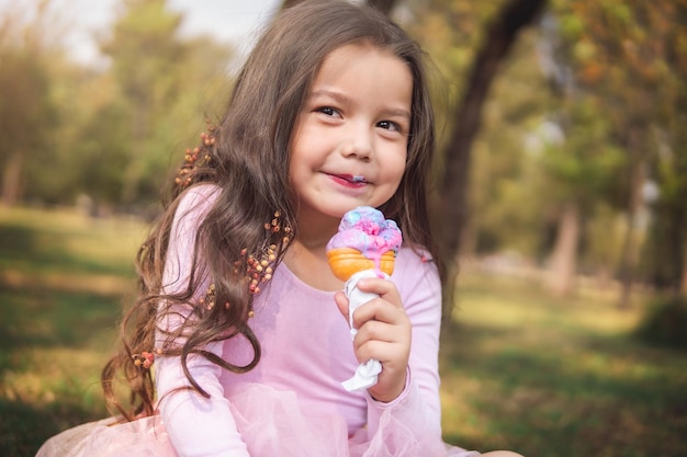 Linda chica rubia de pelo rizado comiendo un buen helado en el concepto del parque del día de los niños