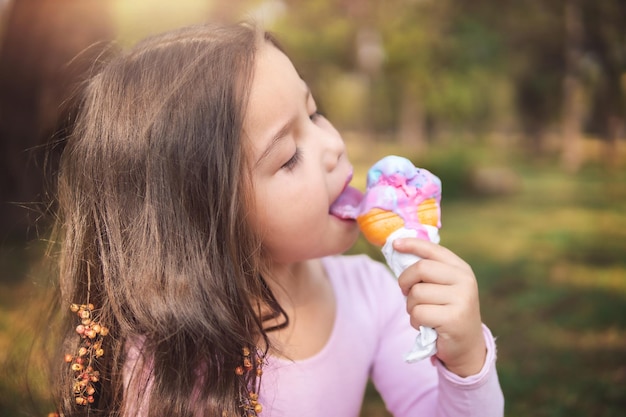 Linda chica rubia de pelo rizado comiendo un buen helado en el concepto del parque del día de los niños