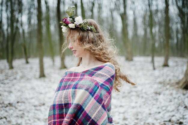 Linda chica rubia rizada con corona en cuadros cuadros en bosque nevado en día de invierno.