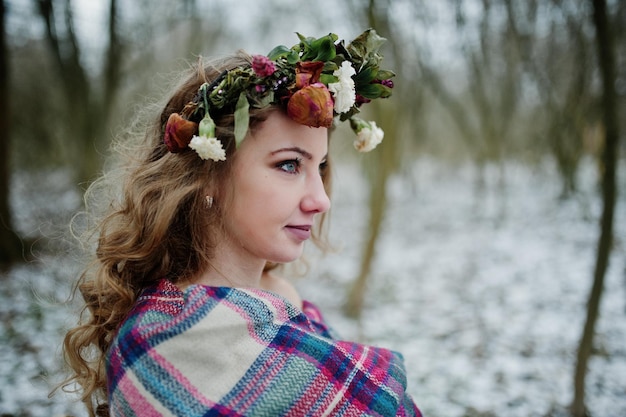 Linda chica rubia rizada con corona en tela escocesa a cuadros en el bosque nevado en el día de invierno
