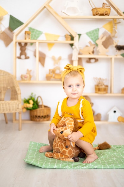 Linda chica saludable jugando con juguetes educativos de madera en una luminosa y acogedora habitación infantil en casa con el telón de fondo de una casa de madera sentada sobre una lujosa jirafa