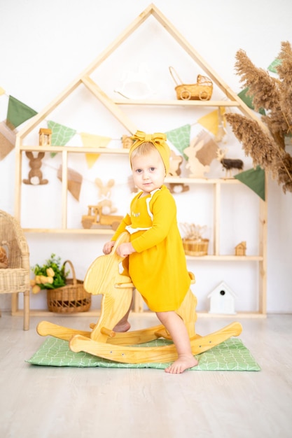 Linda chica sana jugando con juguetes educativos de madera en una luminosa y acogedora habitación infantil en casa con el fondo de una casa de madera sentada en un juguete mecedor de madera
