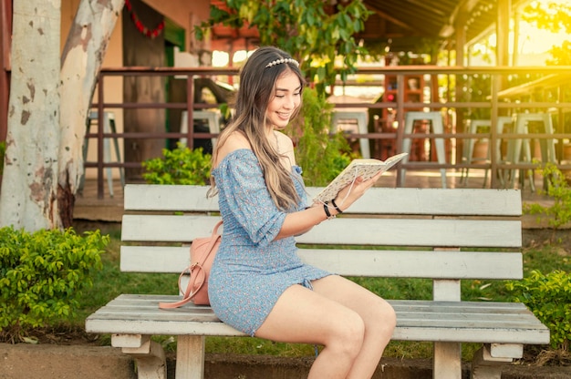 Una linda chica sentada en un banco leyendo un libro bastante joven chica latina leyendo un libro en un banco