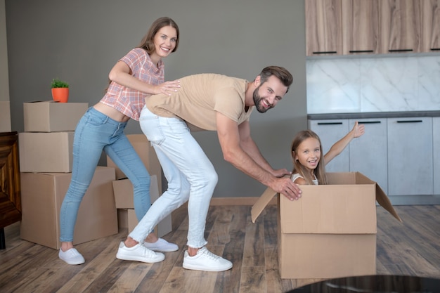 Linda chica sentada en una caja y divertirse con sus padres