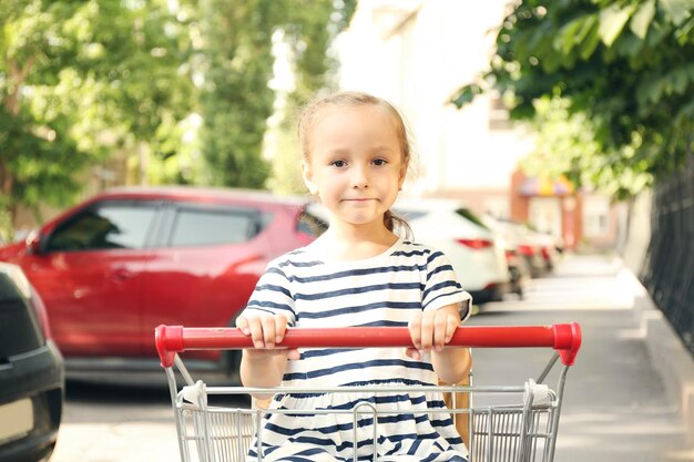 Linda chica sentada en carrito de compras con paquete de productos al aire libre